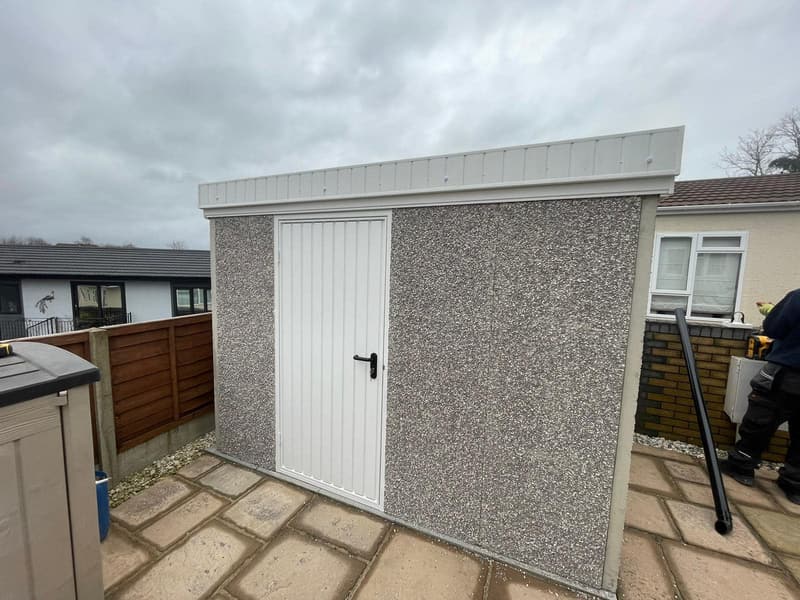 Pent-roof concrete shed in spar finish with white personnel door on a paved base